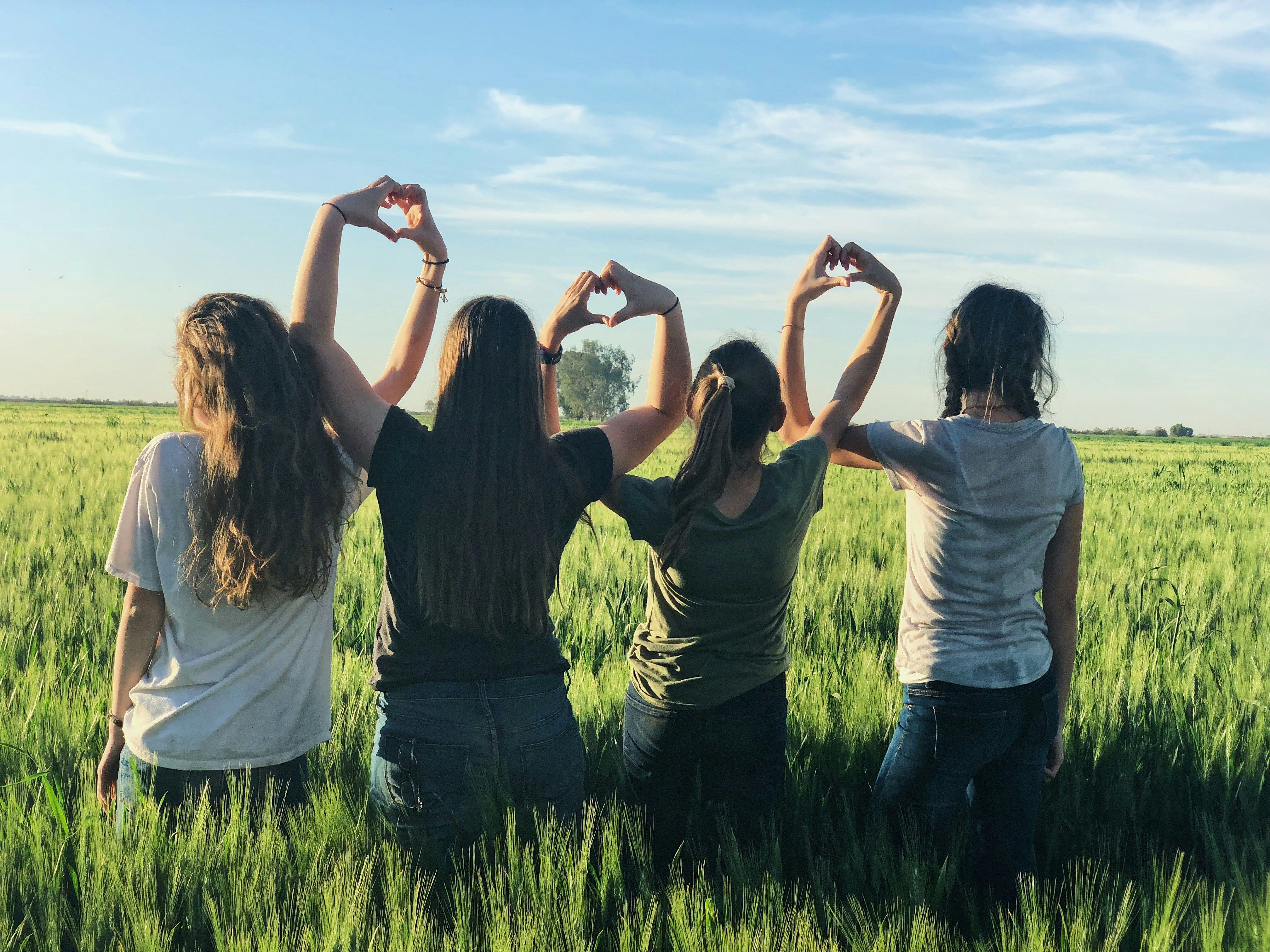 Vier Mädchen stehen auf einem Feld und Formen mit ihren Händen drei Herzen.