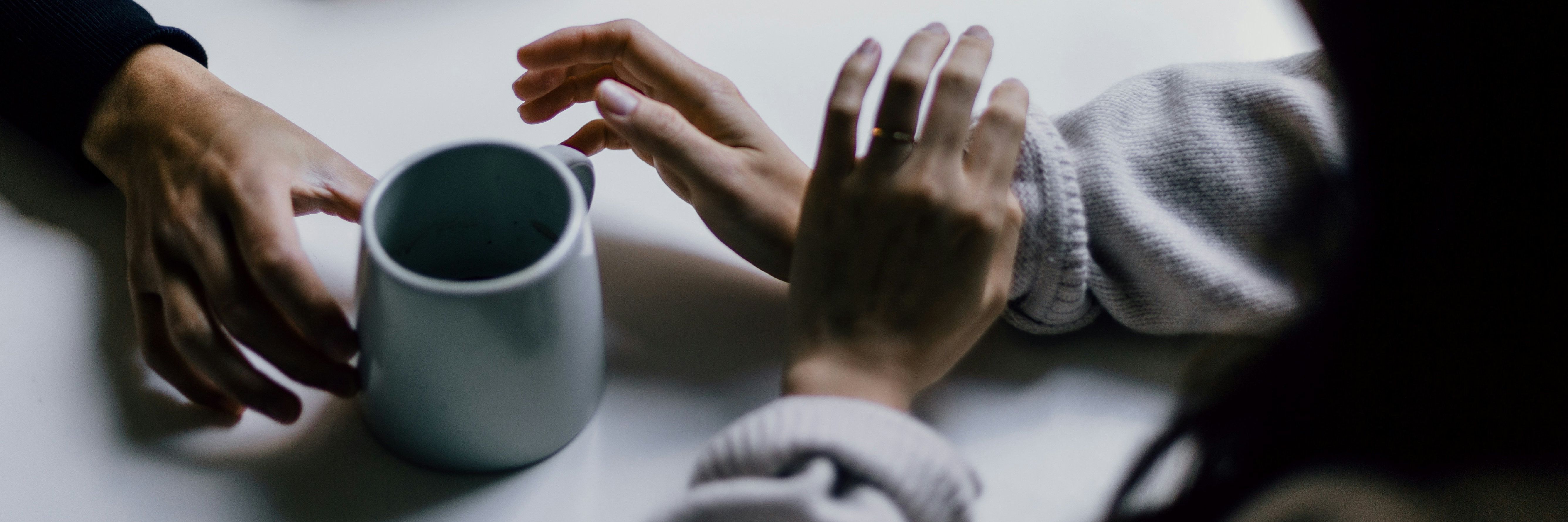 Hände von zwei Personen in einem Gespräch mit einer Tasse Kaffee.
